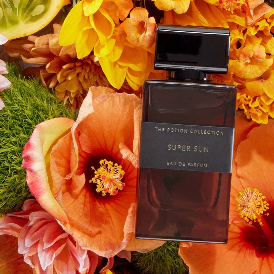 Perfume bottle labeled 'Super Sun' surrounded by vibrant flowers