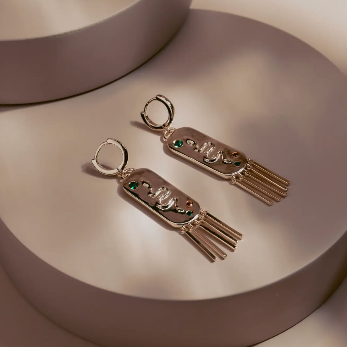 The Serpent Fringe Earrings fuse bold design with fluid movement. Crafted in 14k gold plated over silver, each piece features a raised serpent motif accented with deep green and red stones. The rectangular base flows into fine golden fringe, creating a striking play of texture and light. Confident and sculptural, they bring a touch of power and sophistication to any look.