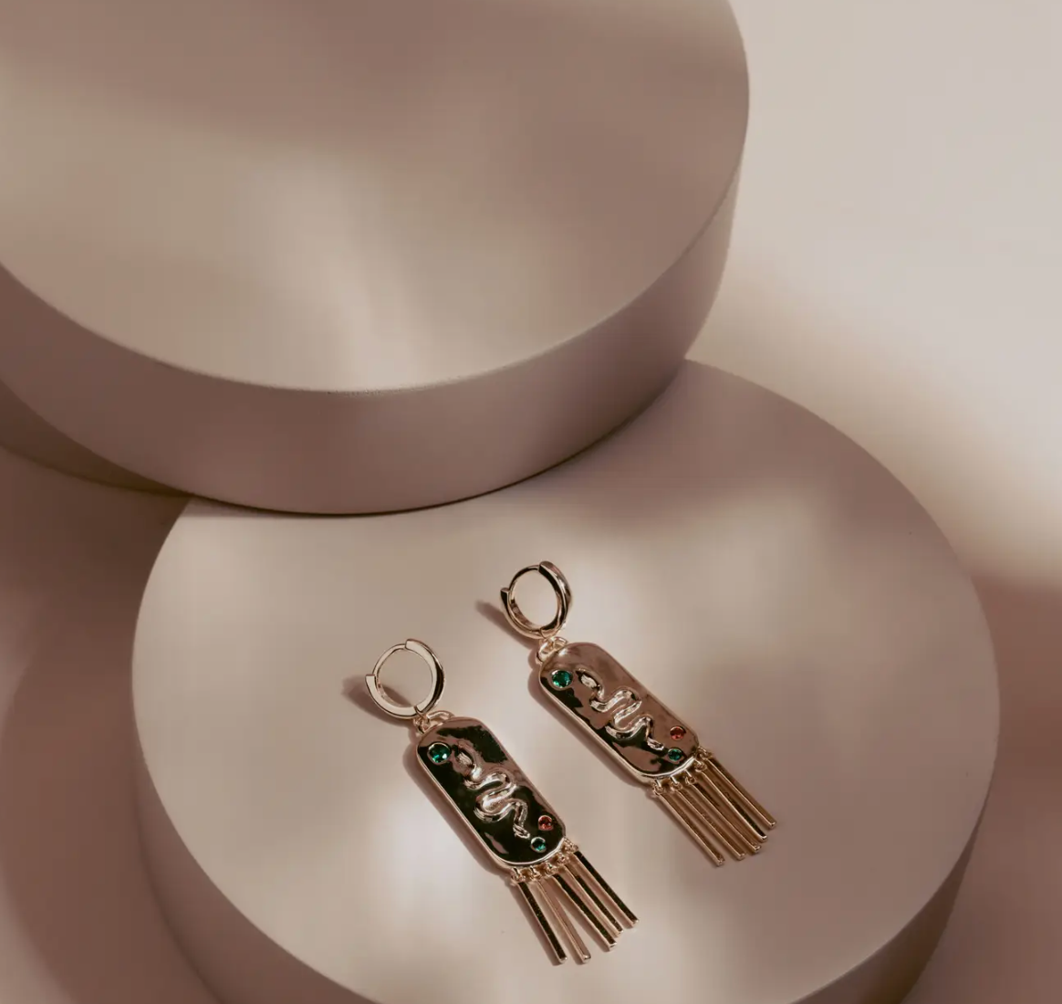 The Serpent Fringe Earrings fuse bold design with fluid movement. Crafted in 14k gold plated over silver, each piece features a raised serpent motif accented with deep green and red stones. The rectangular base flows into fine golden fringe, creating a striking play of texture and light. Confident and sculptural, they bring a touch of power and sophistication to any look.