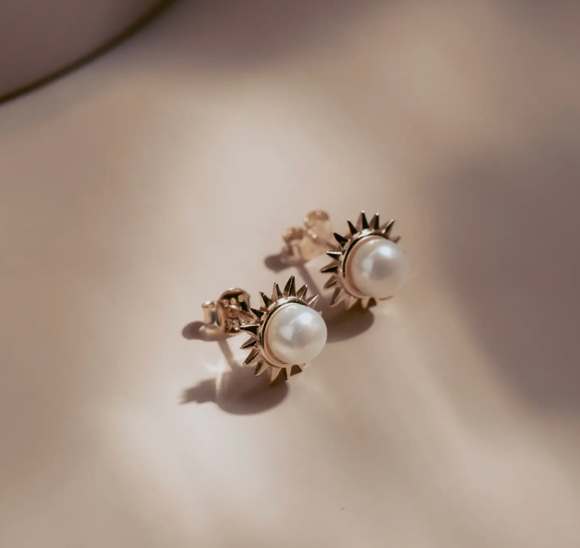 The Solar Pearl Studs capture the warmth of the sun in a timeless design. Each luminous freshwater pearl is framed by a burst of golden rays, crafted in 14k gold plate over sterling silver. Elegant yet bold, they bring effortless sophistication to any look—perfect for day or night.