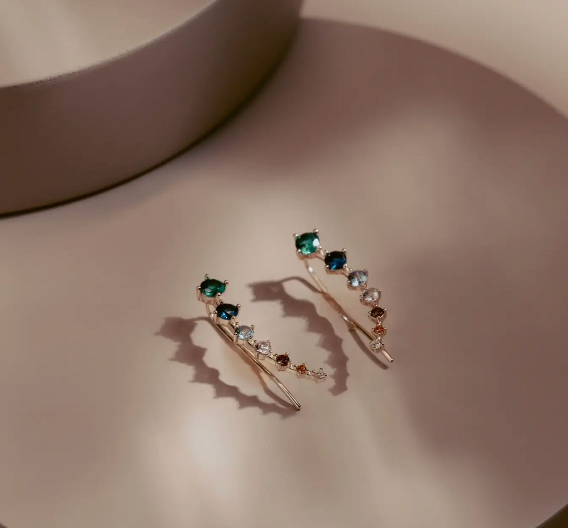 The Celeste Gem Climbers trace the ear with a refined mix of rich green, blue, and neutral stones that catch the light in every direction. Crafted in 14k gold plated over silver, the ascending gradient of faceted gems creates a fluid, modern silhouette. Elegant and effortless, they bring subtle color and quiet sophistication to any look.