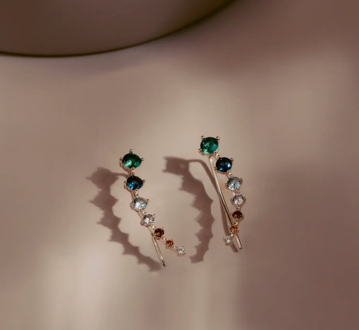 The Celeste Gem Climbers trace the ear with a refined mix of rich green, blue, and neutral stones that catch the light in every direction. Crafted in 14k gold plated over silver, the ascending gradient of faceted gems creates a fluid, modern silhouette. Elegant and effortless, they bring subtle color and quiet sophistication to any look.