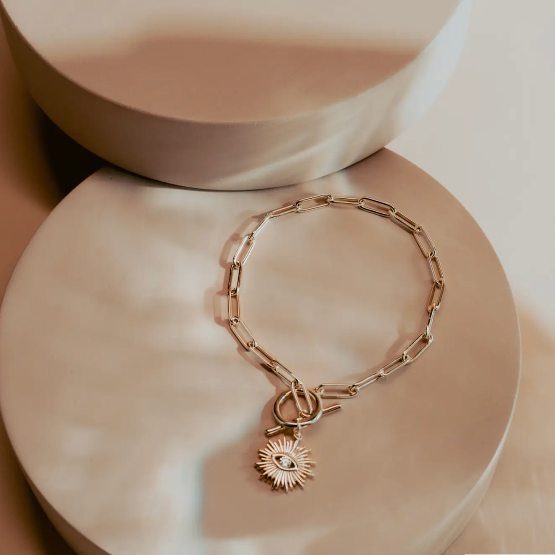 The Golden Eye Bracelet blends sleek design with symbolic detail. Crafted in 14k gold plated over silver, it features a bold paperclip chain and a front toggle clasp accented by a radiant sunburst charm set with a clear crystal eye. Polished and versatile, it brings a touch of strength and modern refinement to any style.