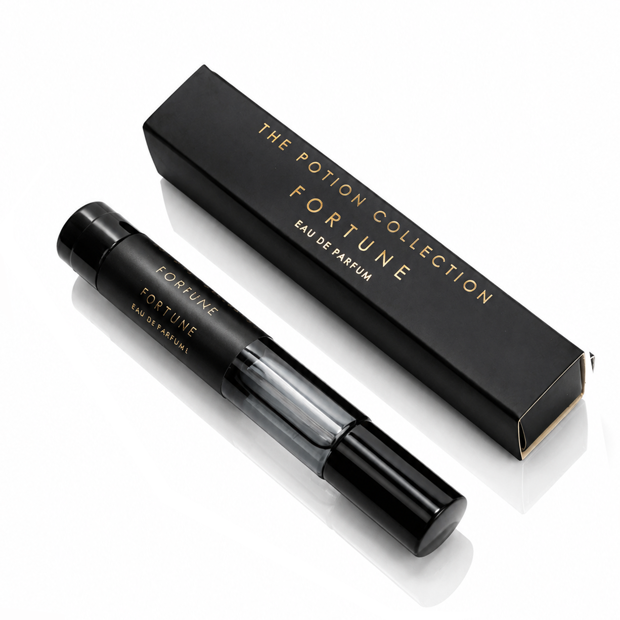 A black perfume rollerball bottle with gold lettering next to its black packaging box, both from The Potion Collection Fortune Eau de Parfum, on a white reflective background.