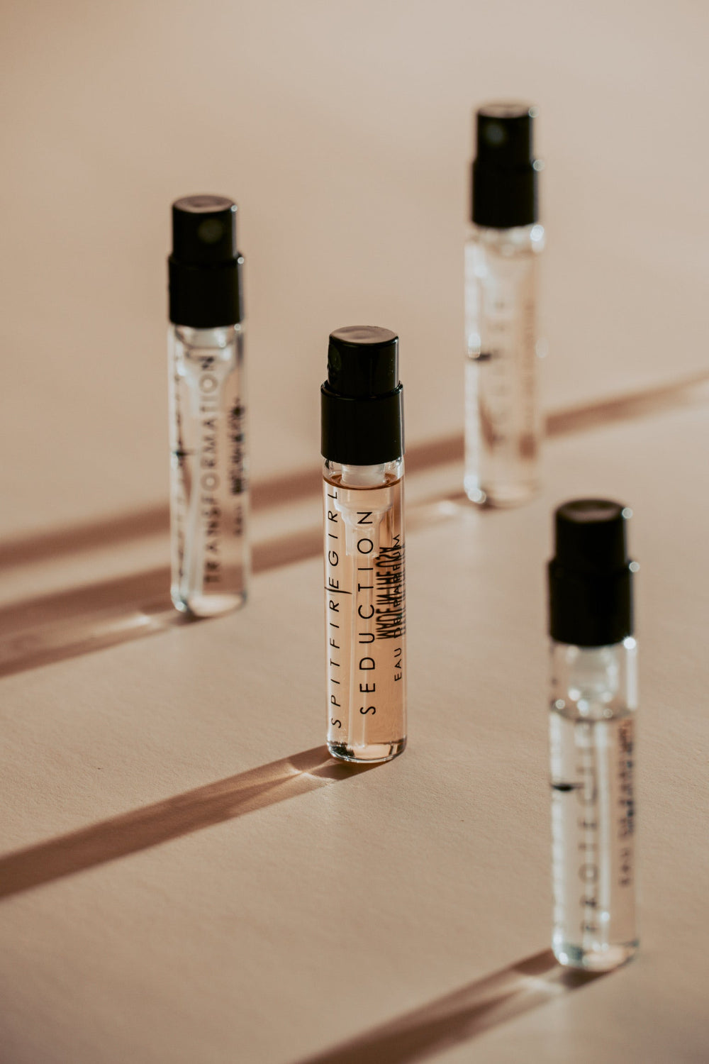 Four small perfume bottles with black caps on a beige surface