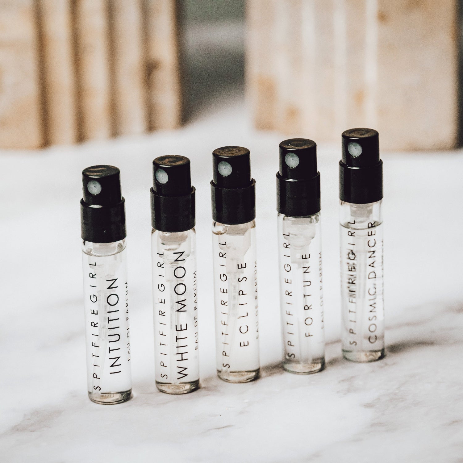 Five small perfume bottles with black caps on a marble surface