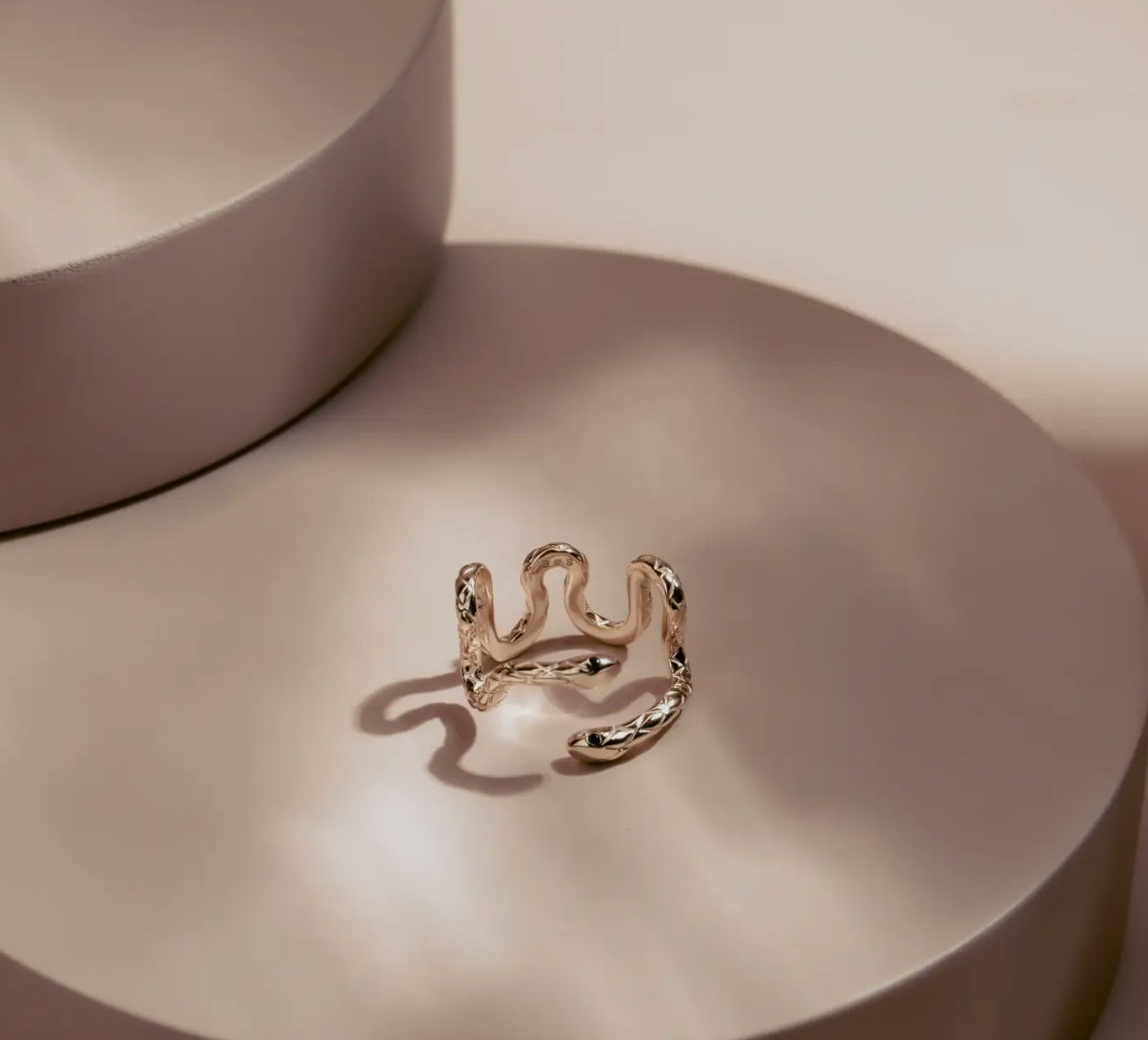 Sleek and hypnotic, the Serpent Coil Ring embodies power and transformation. Crafted in gleaming 14k gold plate over sterling silver, the coiled design wraps gracefully around the finger, ending in twin sculpted snake heads with dark alluring eyes. Adjustable for a perfect fit.
