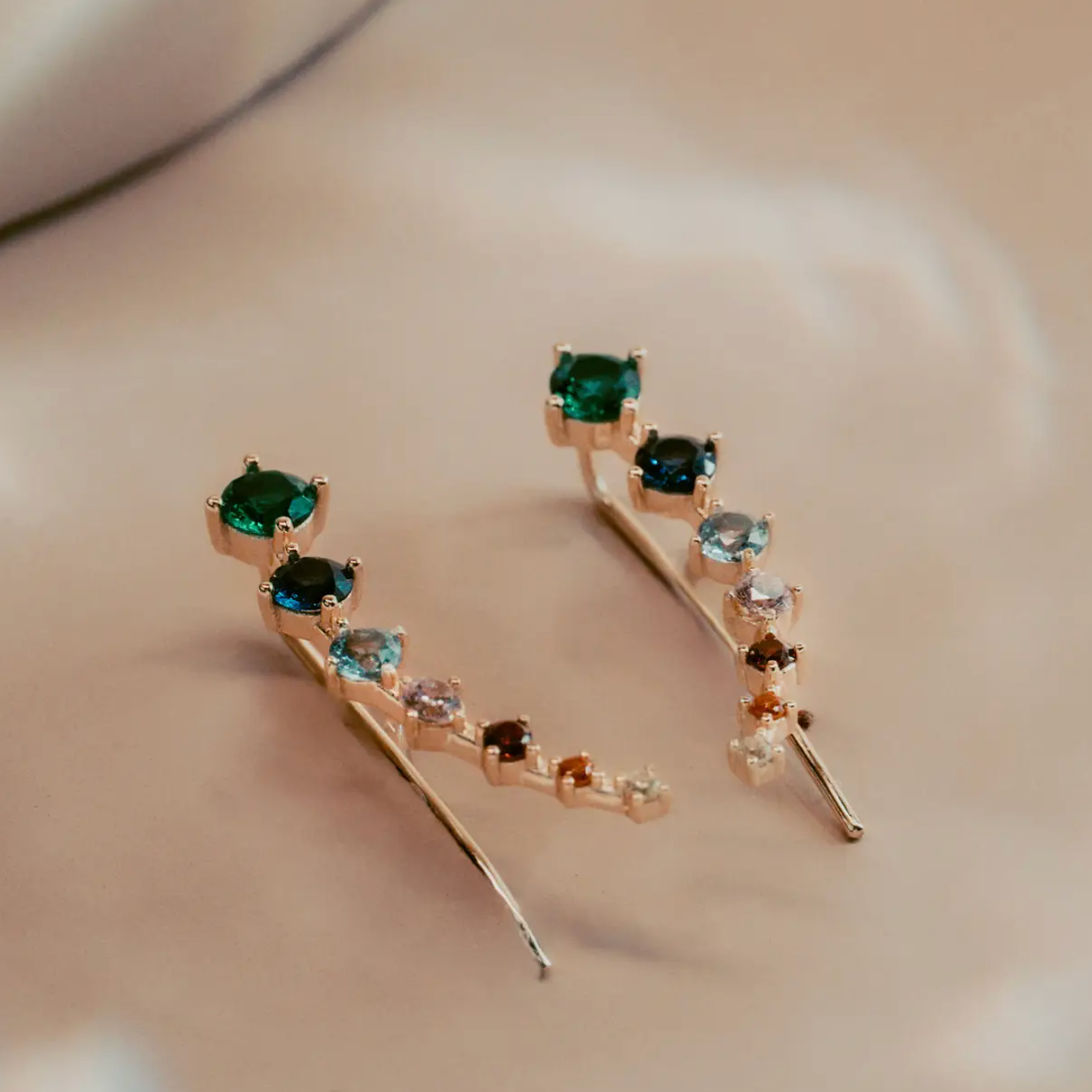 The Celeste Gem Climbers trace the ear with a refined mix of rich green, blue, and neutral stones that catch the light in every direction. Crafted in 14k gold plated over silver, the ascending gradient of faceted gems creates a fluid, modern silhouette. Elegant and effortless, they bring subtle color and quiet sophistication to any look.