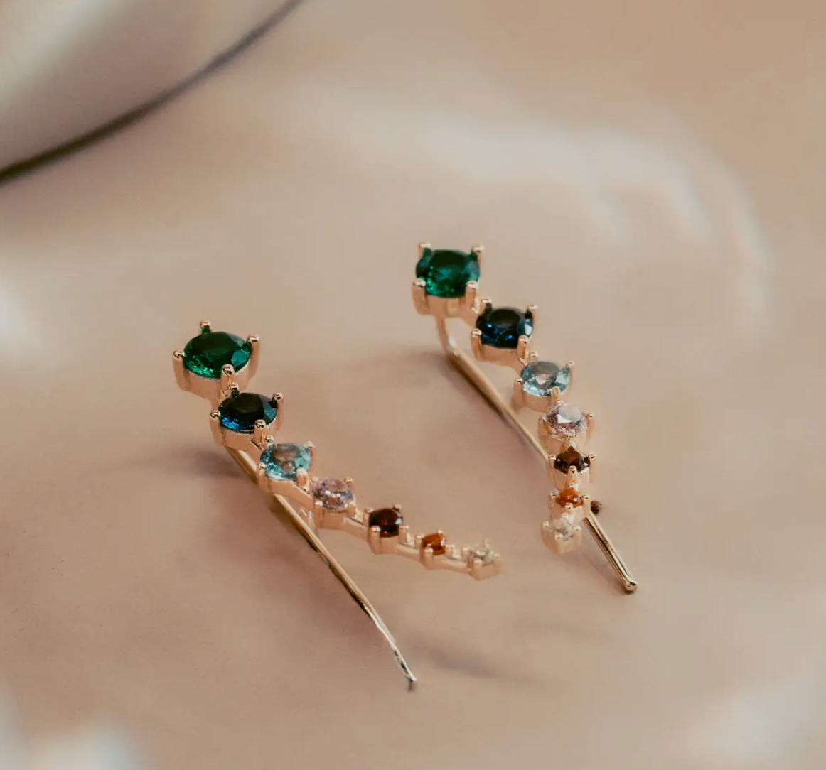The Celeste Gem Climbers trace the ear with a refined mix of rich green, blue, and neutral stones that catch the light in every direction. Crafted in 14k gold plated over silver, the ascending gradient of faceted gems creates a fluid, modern silhouette. Elegant and effortless, they bring subtle color and quiet sophistication to any look.