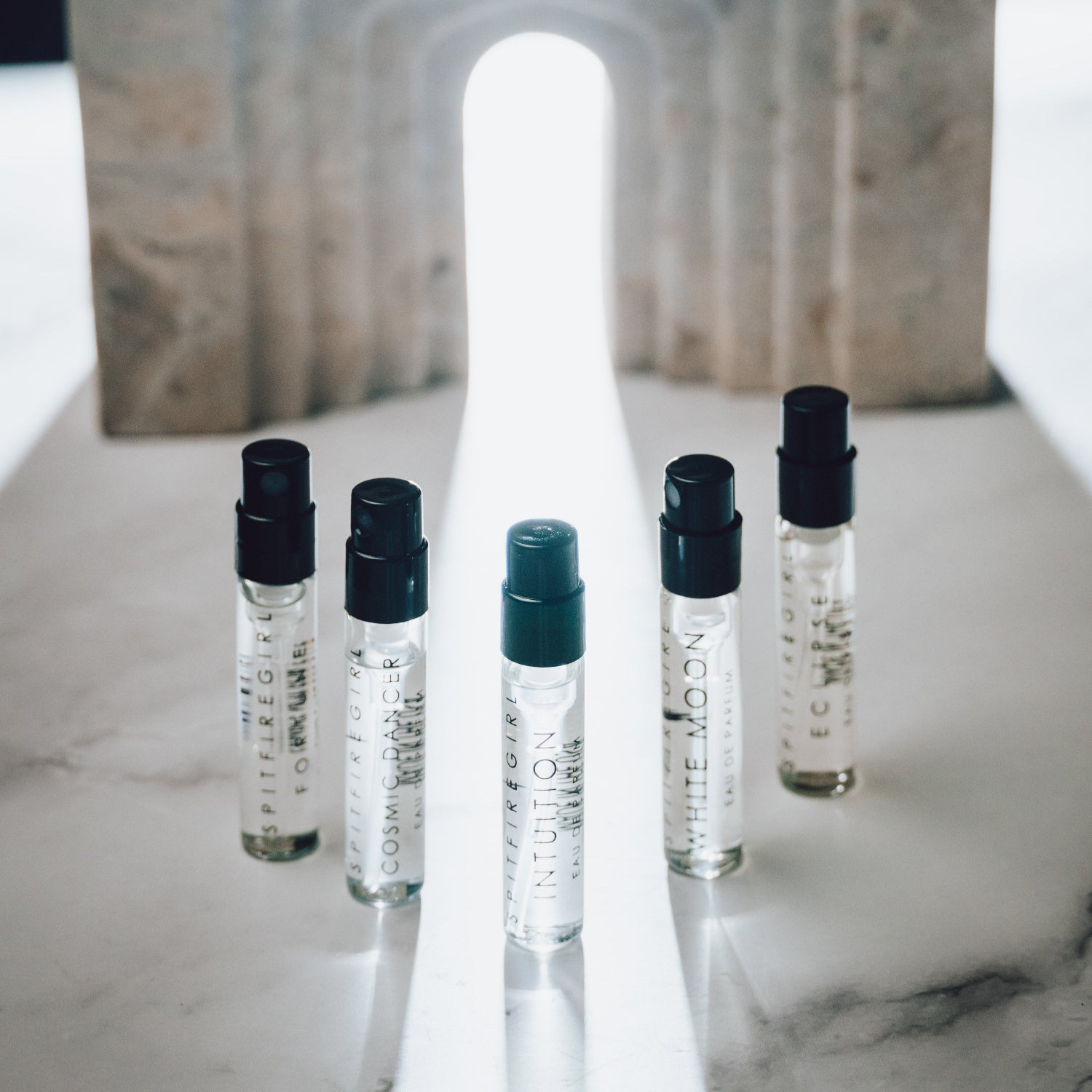 Set of small perfume bottles with black caps on a marble surface